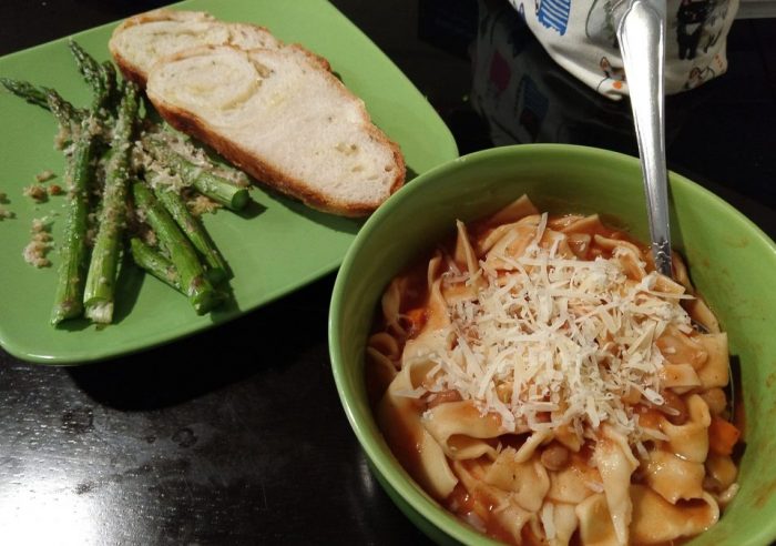 a bowl of taglioli and bean soup, topped with shredded cheese, and a plate with two slices of gruyère loaf plus roasted asparagus