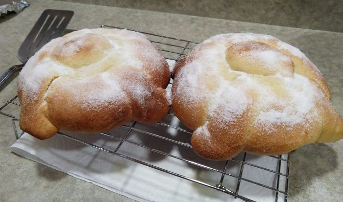 two loaves of pan de muerto covered in white sugar, on top of a wire rack