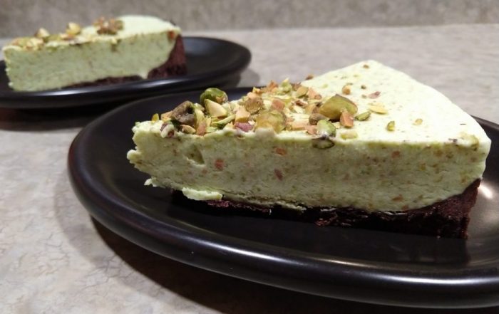 two slices of pistachio mousse tart on small plates, with a focus on the slice in the foreground. A thin shortbread base topped with light-green pistachio mousse and chopped pistachios