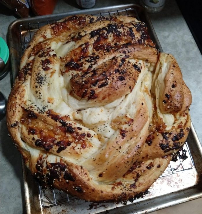 a large loaf of bread, braided and wrapped in a cricle, with exposed bits of carmelized onion and cheese filling