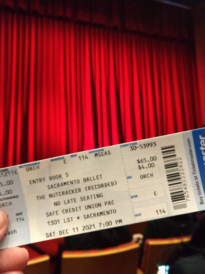 A ticket for the Sacramento Ballet's Nutcracker performance, held up in front of the red theater curtain