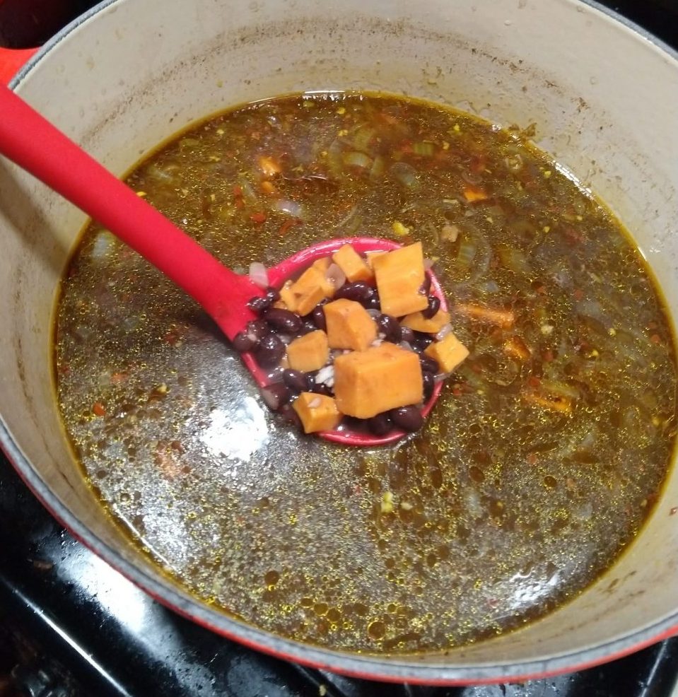 a large pot of soup. The photo focuses on a ladle full of beans and sweet potato chunks. The soup underneath just looks soup and you can't tell what's in it.