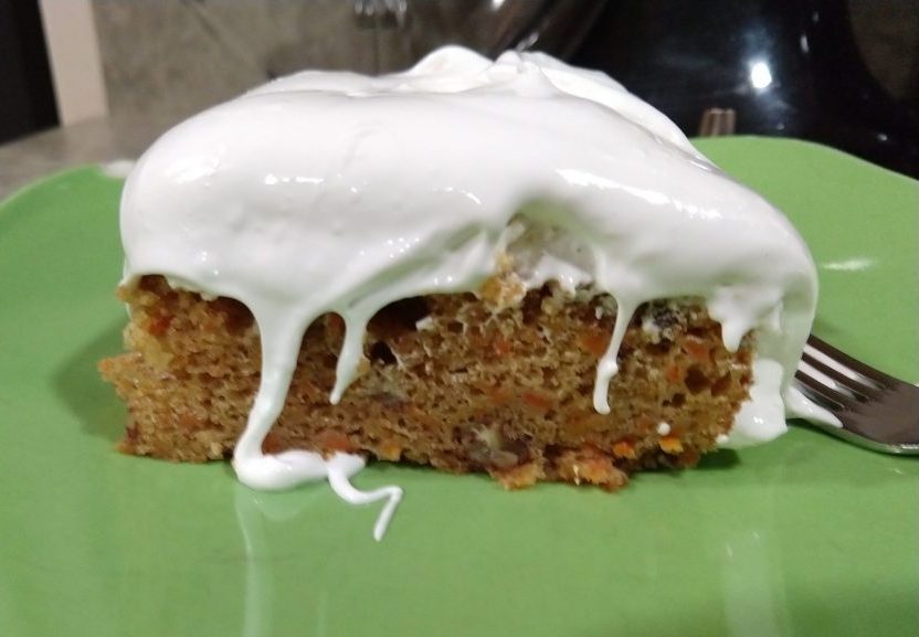 a slice of carrot cake on a green plate. Meringue is heaped on top and some of it is dripping down.