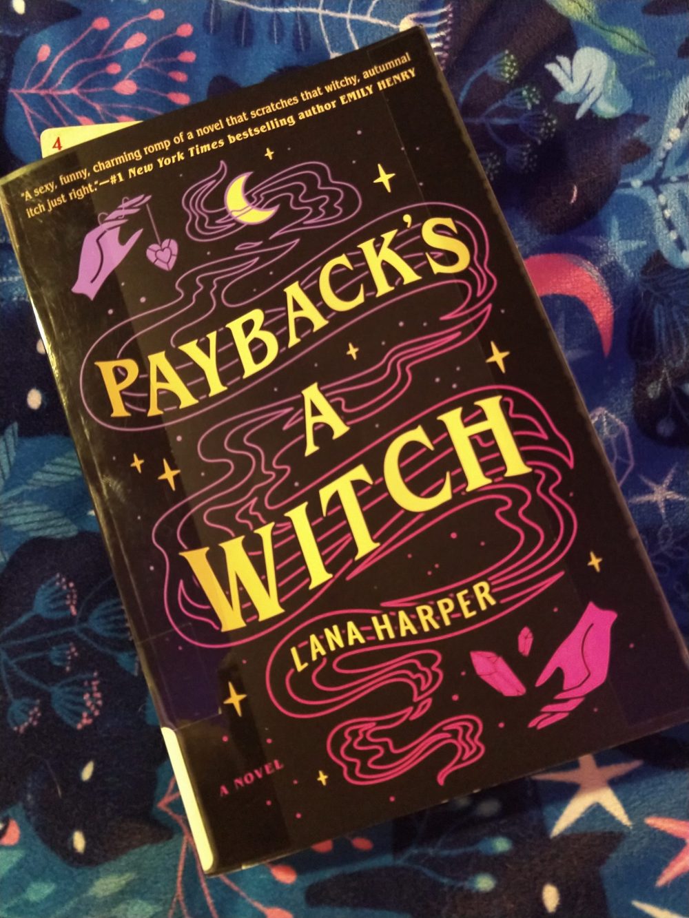 paperback book: Payback's a Witch. Cover is black with gold text and pink and purple witchy imagery