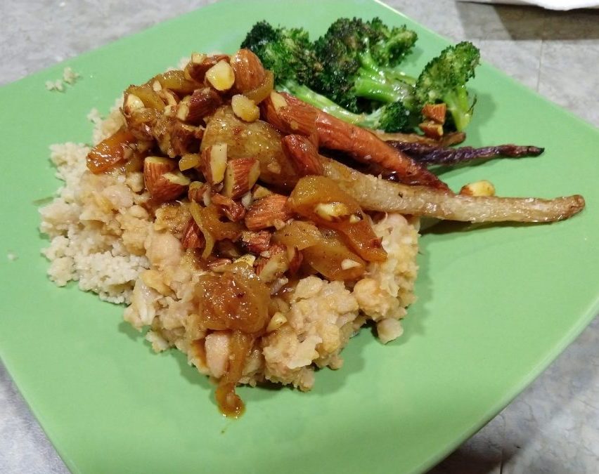a plate layered with cous cous, smashed chickpeas, an almond/dried apricot topping, roasted carrots and broccoli