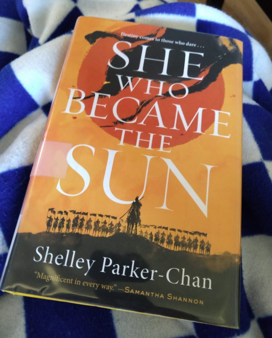book: She Who Became the Sun. cover is a yellow-oange with the silhouettes of soldiers on horses along the bottom