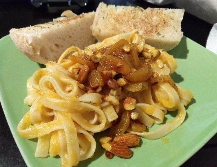 a plate of pasta coated in butternut squash puree and topped with an almond and apricot mix. There's also garlic bread.