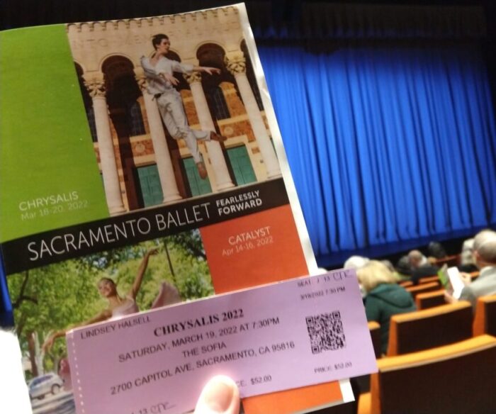 a program and ticket for the Chrysalis show at the Sacramento Ballet in the foreground with a blue curtain closed over the stage in the background