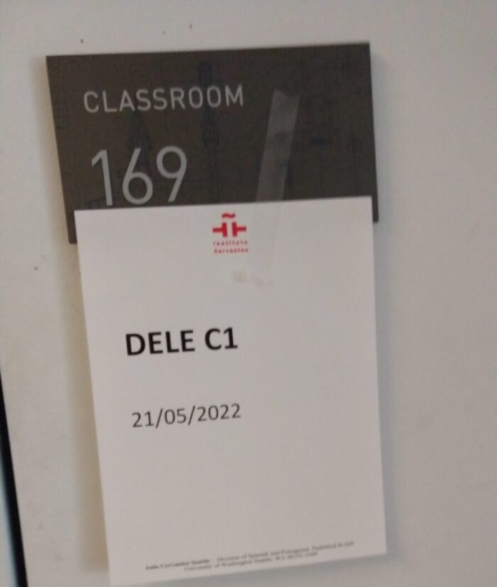 a sign in front of a classroom door with a room number and a sign taped on that says "DELE C1 21/05/2022"