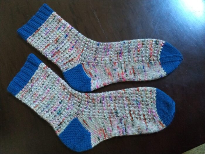 socks in a greyish yarn with pops of varigated color, blue cuff, heel and toe