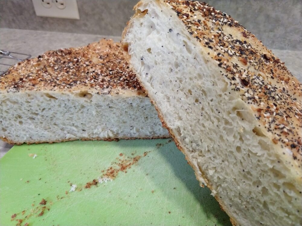 a round loaf of bread covered in everything bagel seasoning. The photo shows the cross-section of the loaf.