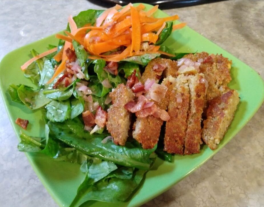 an attempt at a fancy salad. A plate of spinach topped with carrot ribbons, sliced split pea fritters, and bacon vinaigrette