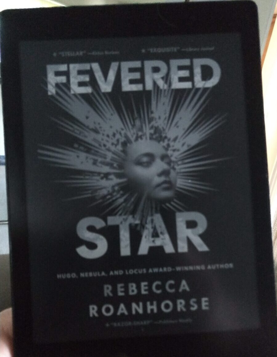 book cover for Fevered Star shown in greyscale on kobo ereader. Cover featurse a woman's face with burts of light radiating out in all directions