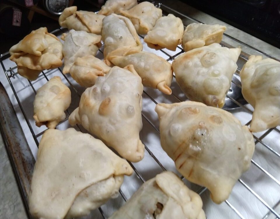 freshly fried samosas on a cooling rack. The samosas have bubbled up and browned with frying
