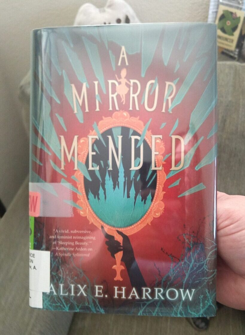 hardback book from the library: A Mirror Mended by Alix E Harrow. The cover shows a large, ornate handmirror with the reflection of a castle inside.