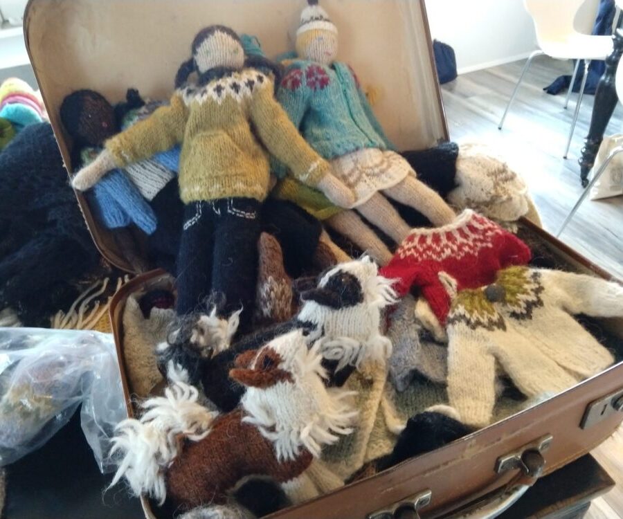 a vintage suitcase full of knitted dolls and their traditional icelandic seaters. There are also two knitted sheepdogs nestled into the suitcase in the foreground.