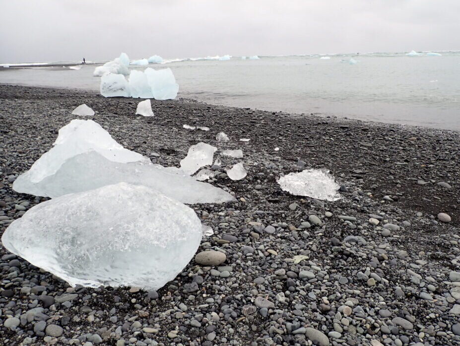 smaller chunks of glacier ice on a rocky, black beach.
