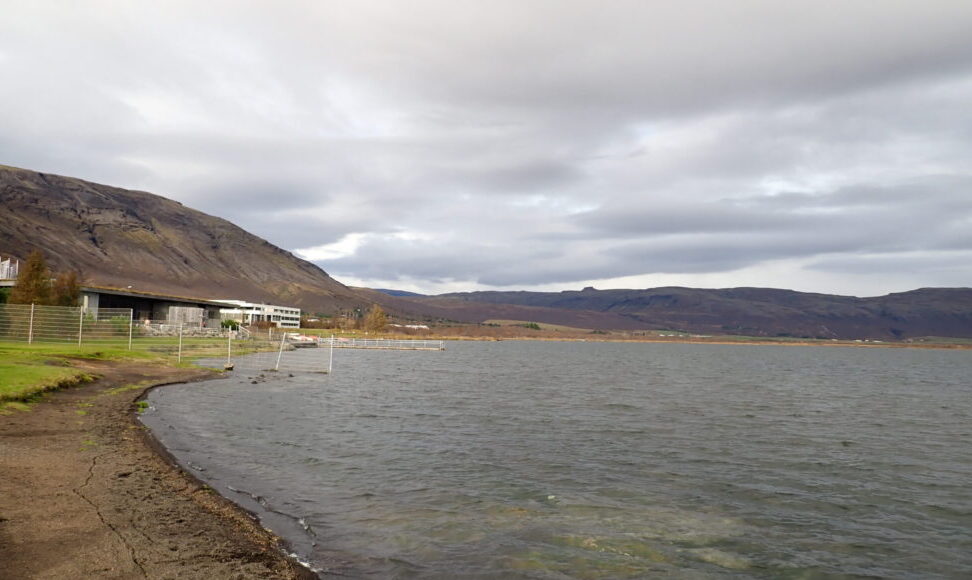 A lake (Laugarvatn) with a view of the bathing facility to one side. Mountains ring the lake.