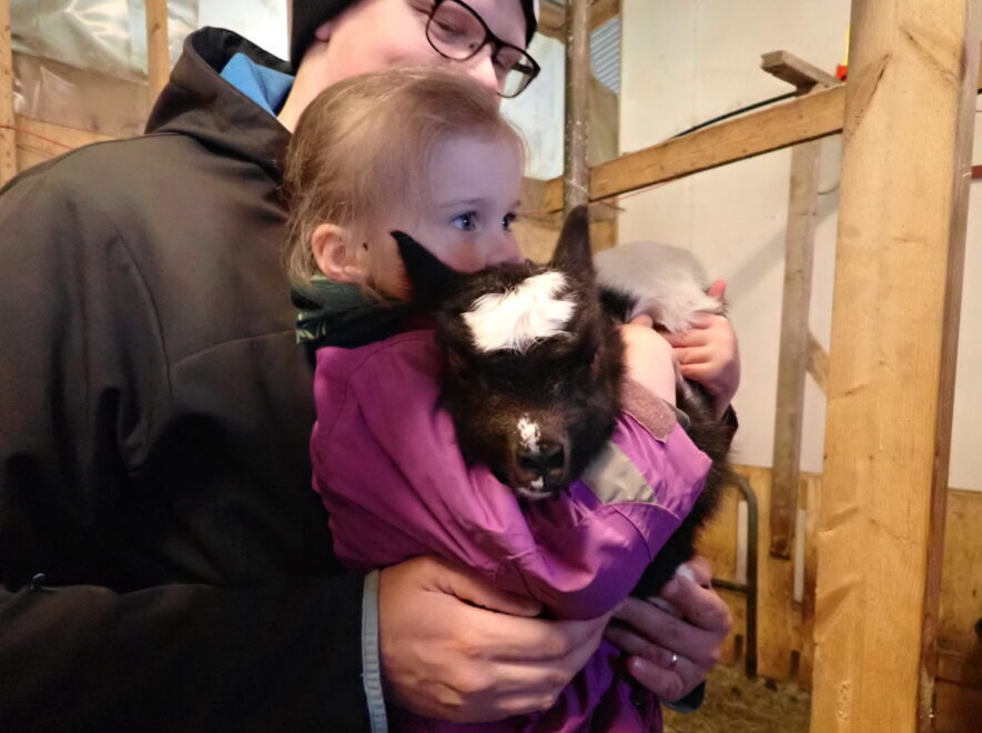 a man holding a small child holding a goat. The goat is black and white and generally very cute