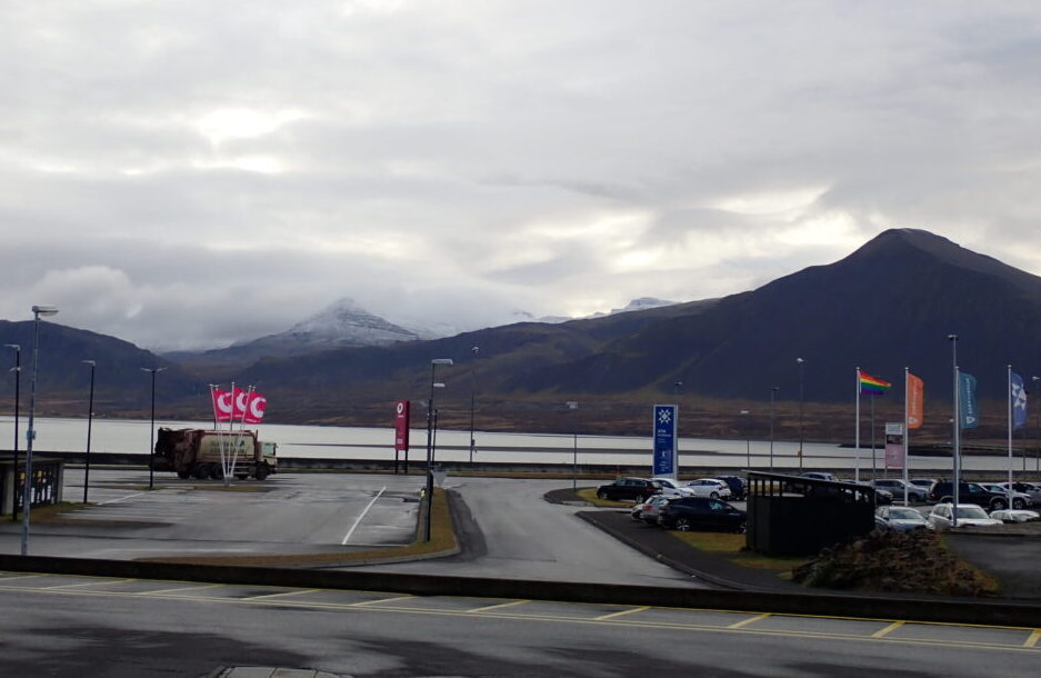 A gas station parking lot but there are snow-capped mountains in the background