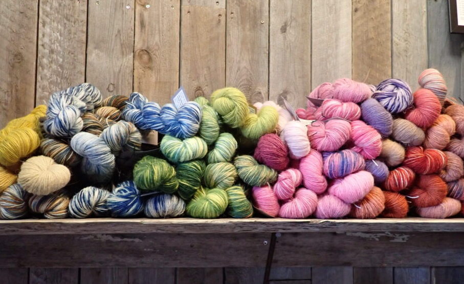 A shelf of skeins of yarn in a rainbow of colors, which contrasts nicely against a natural wood wall.