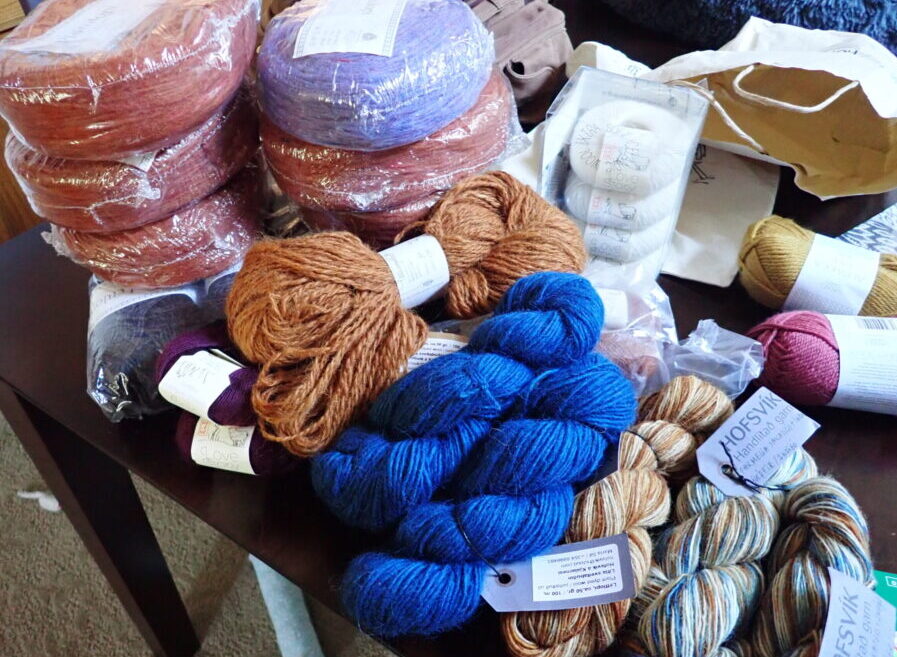 a whole bunch of yarn on a table including several rounds of Icelandic plötulopi, smaller skeins of Love Story yarn, and several skeins of plant-dyed yarns