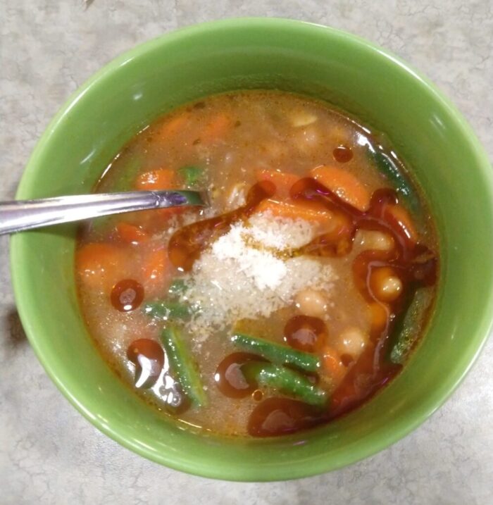 a bowl of soup studded with chickpeas, carrots, and green beans, and topped with parmesan and chili oil