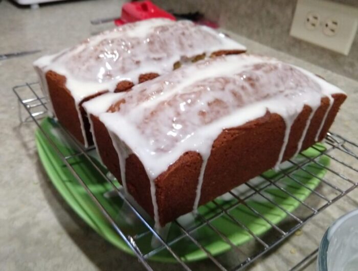 two loaf-shaped orange cakes on a wire rack. They are coated and dripping with an icing glaze.