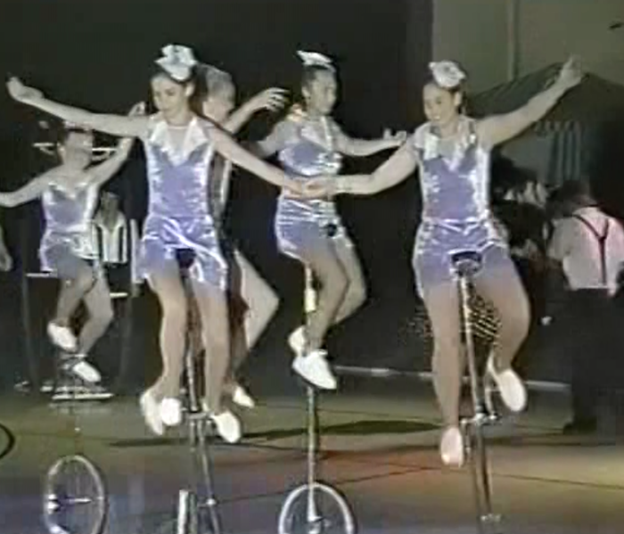 a group of teenage girls riding five-foot tall unicycles in a formation