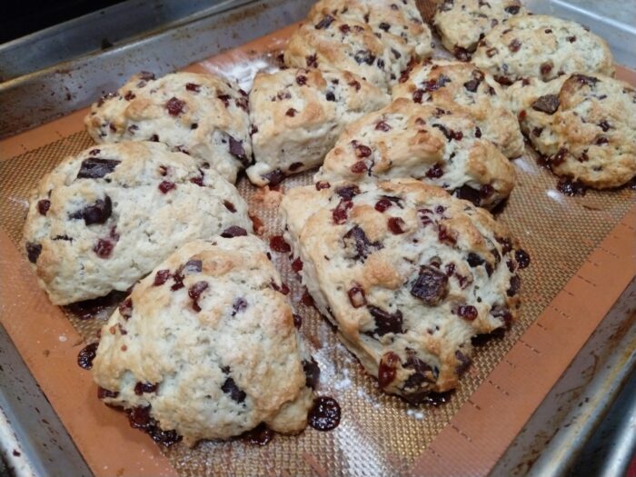 a sheet pan of freshly baked scones that are full of rasberry bits and chocolate chunks