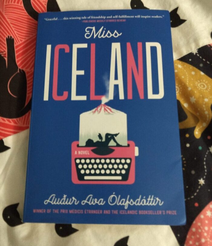 paperback book: Miss Iceland. Cover design features a pink typewriter, with the silhouette of a woman lying down and reading a book on top of it, and a volcano behind that.