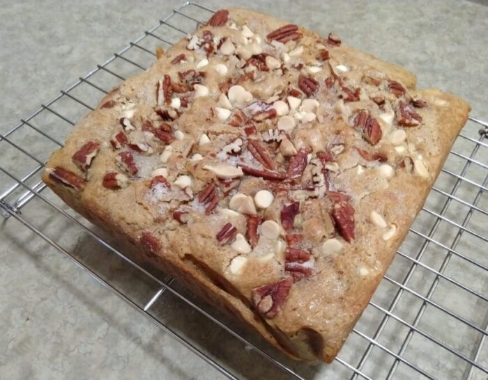 a square cake covered in pieces of pecan and white chocolate chips