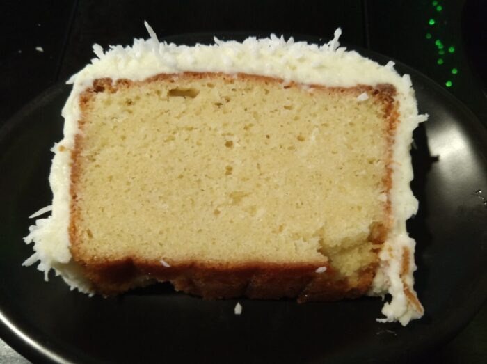a slice of coconut cake. It's a loaf cake covered in a layer of cream cheese frosting, which is topped with shreds of coconut