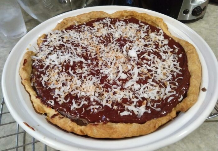 a whole pie topped with chocolate ganache and toasted coconut, still in the pie pan