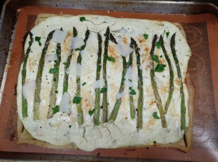 a puff pastry tart covered with a cheesy mixture and topped with asparagus spears