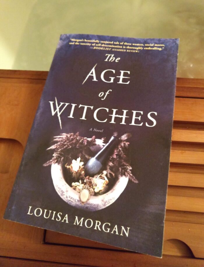 book: The Age of Witches. The book is lying on a bath tray and water is visible in the background