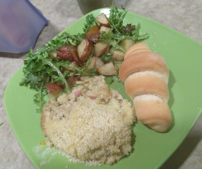 a dinner plate with beans au gratin, and roasted potato and arugula salad, and a crescent roll