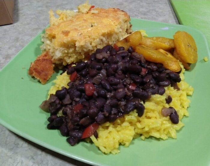 a plate of black beans and rice, fried plantains, and corn spoon bread