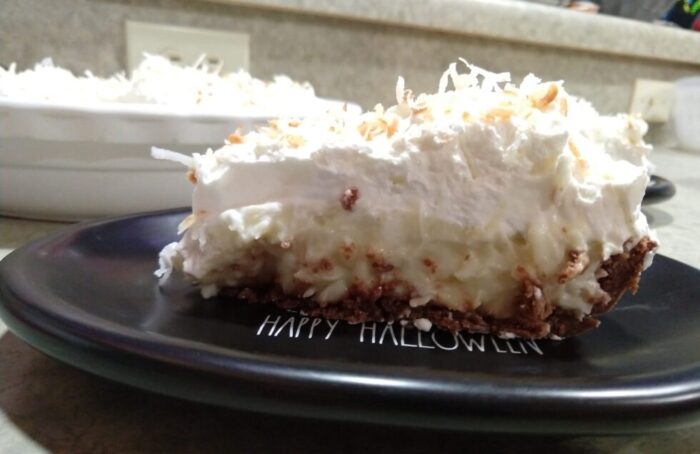 a slice of coconut cream pie showing a cookie base, coconut pudding middle, and a big pile of whipped cream on top