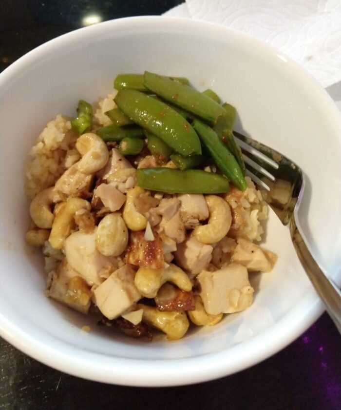 a bowl of tofu and cashews and snap peas over rice