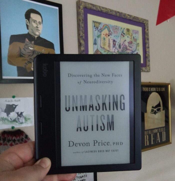 book cover for Unmasking Autism shown on kobo ereader. Various wall art visible in the background