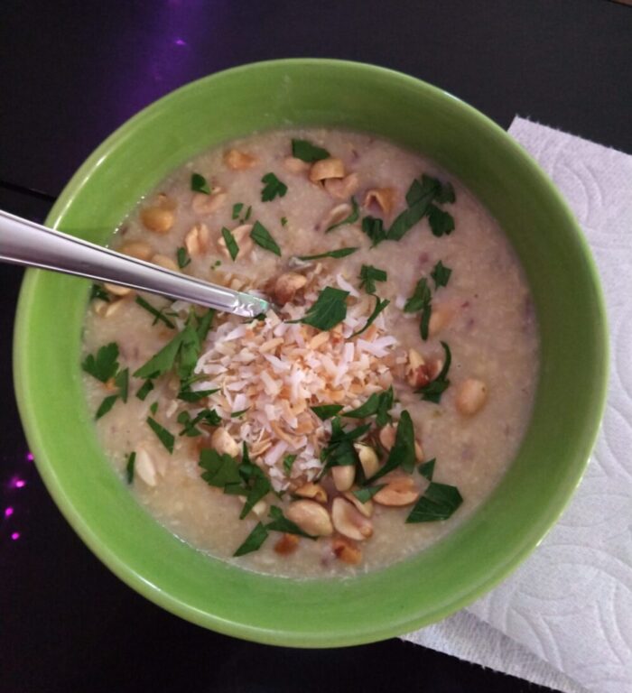 a bowl of coconut corn soup topped with toasted coconut, peanuts, and parsley