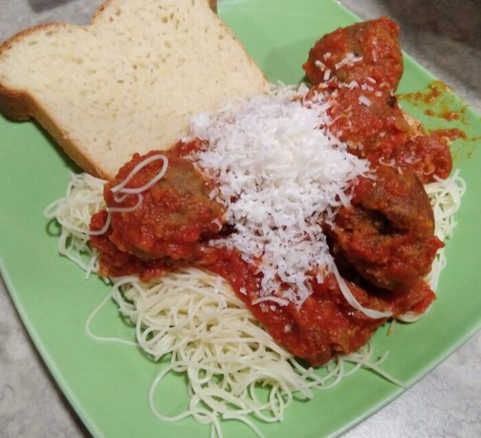 A pile of noodles topped with lentil meatballs and tomato sauce. A slice of bread is next to the pasta