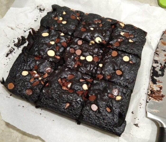 a square of brownies cut into nine pieces. A variety of chocolate chips dot the top. The brownies are very dark because they use black cocoa powder