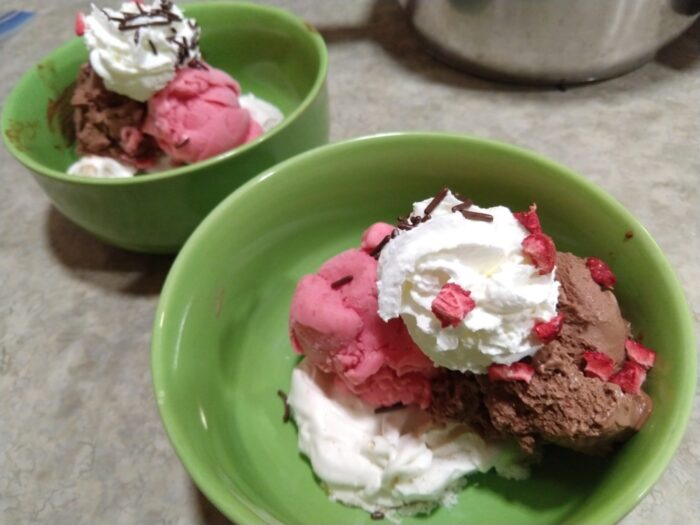 two bowls of ice cream, each with a scoop of strawberry frozen yogurt and of chocolate ice cream. There is a meringue underneath the ice cream and whipped cream on top