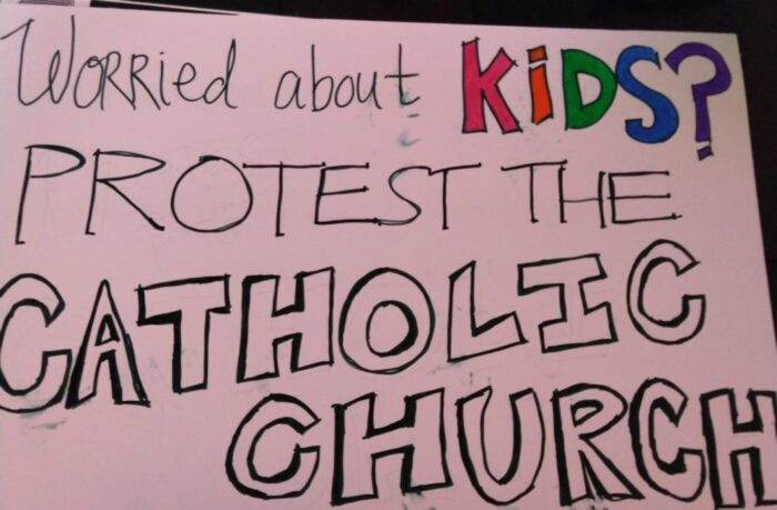 a sign that says "Worried about kids? Protest the Catholic church" in marker