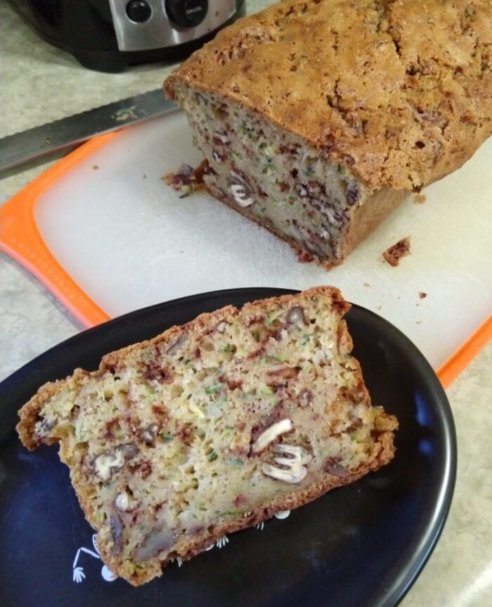 a slice of zucchini bread on a plate with the rest of the loaf on a cutting board