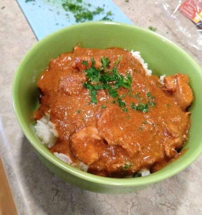 a bowl of butter chicken over rice, topped with chopped parsley