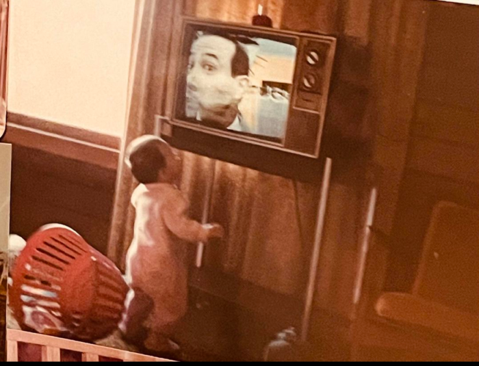 me as a baby, looking up at a TV showing a close up of Paul Reuben's face