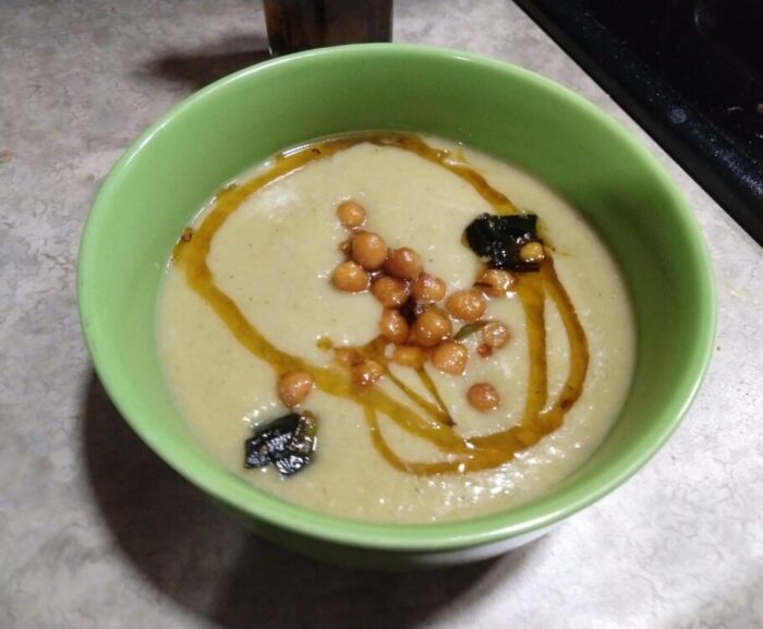 A bowl of smooth soup topped with crispy chickpeas and leeks, plus a swirl of chili oil